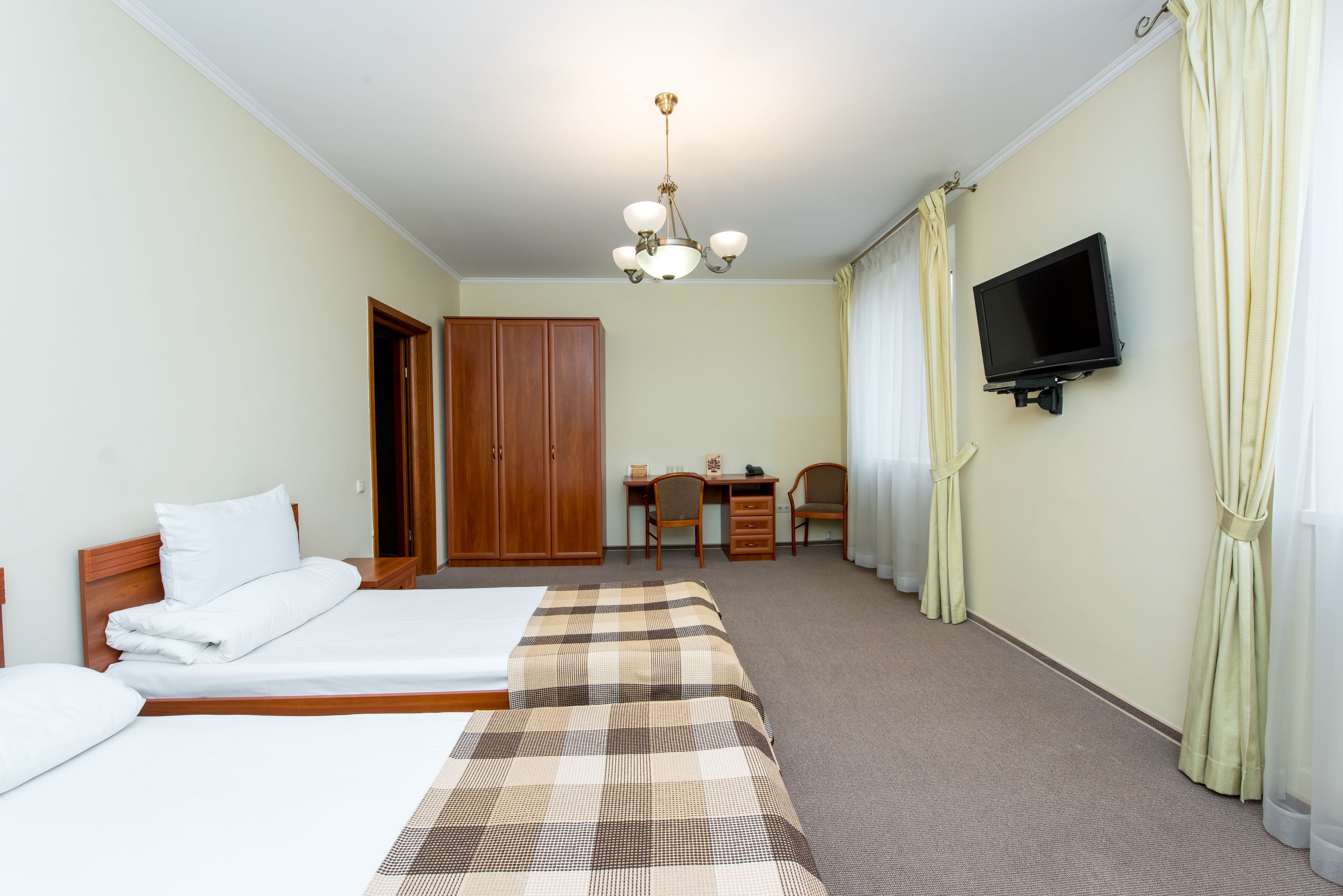 Habitación de hotel con dos camas, un escritorio, una silla, un televisor y un armario.