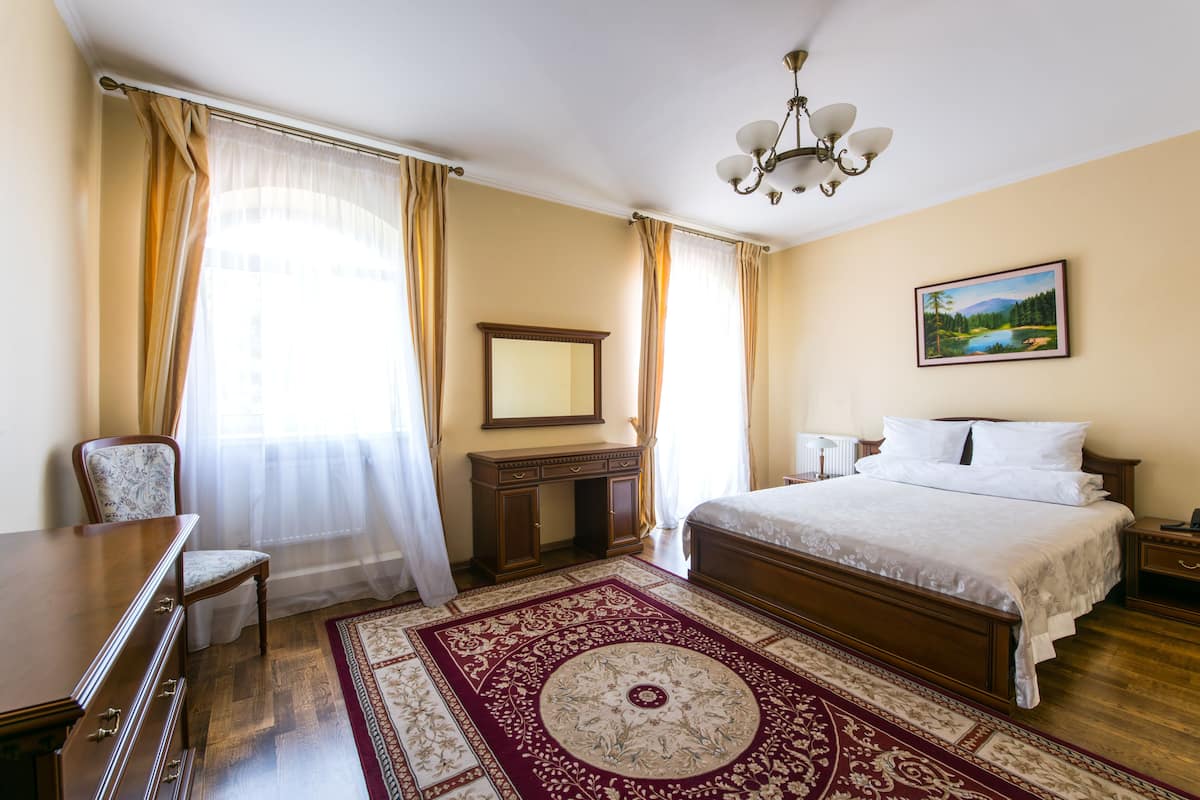A hotel room with a large bed, a wooden dresser, a desk, and a chair.