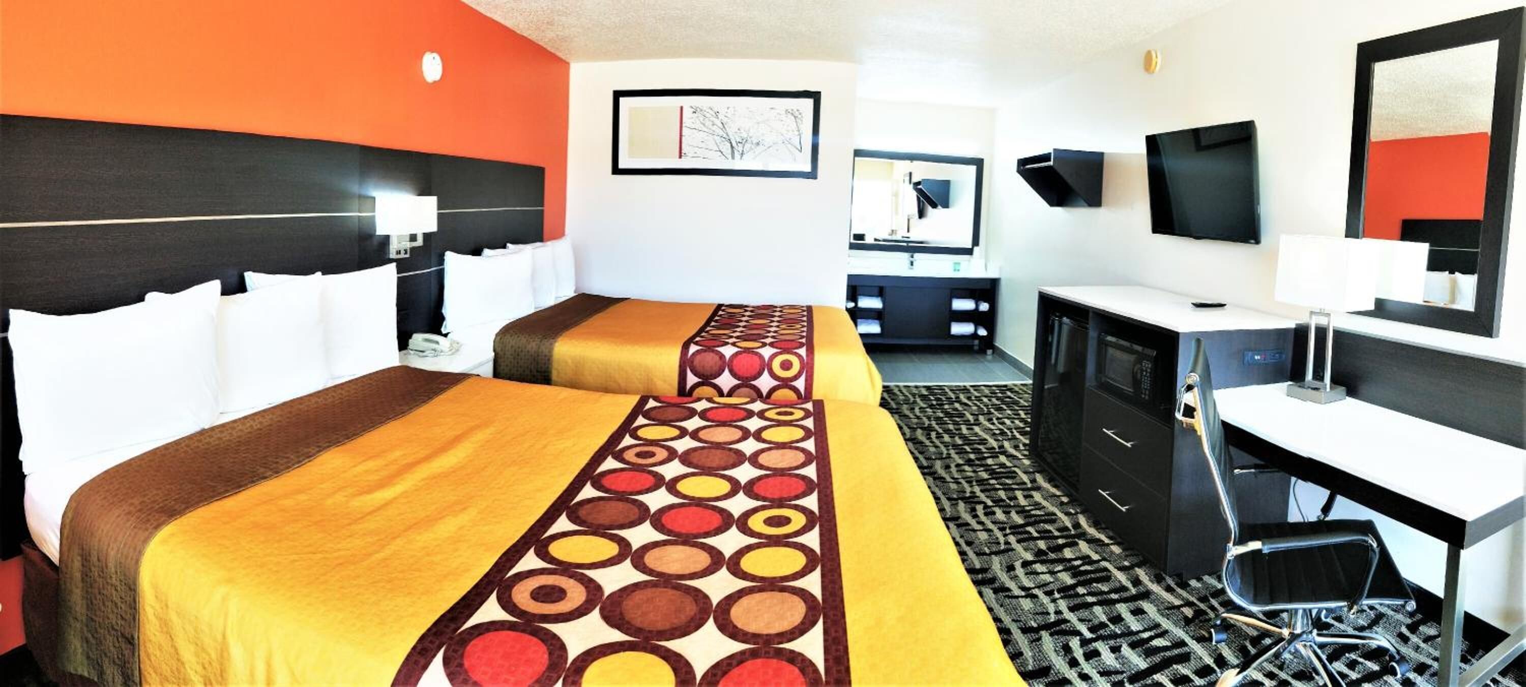 Una habitación de hotel con dos camas, un escritorio, una silla, un televisor y un aparador.
