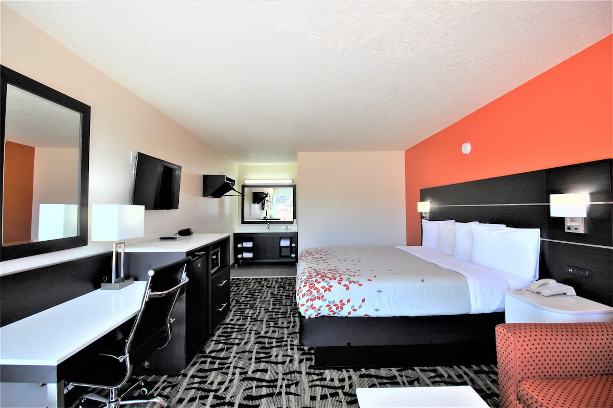 Quarto de hotel com cama, escrivaninha, cadeira, espelho e televisão.