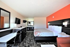 A hotel room with a bed, a desk, a chair, a mirror, and a television. - Travel Inn (Eutaw)