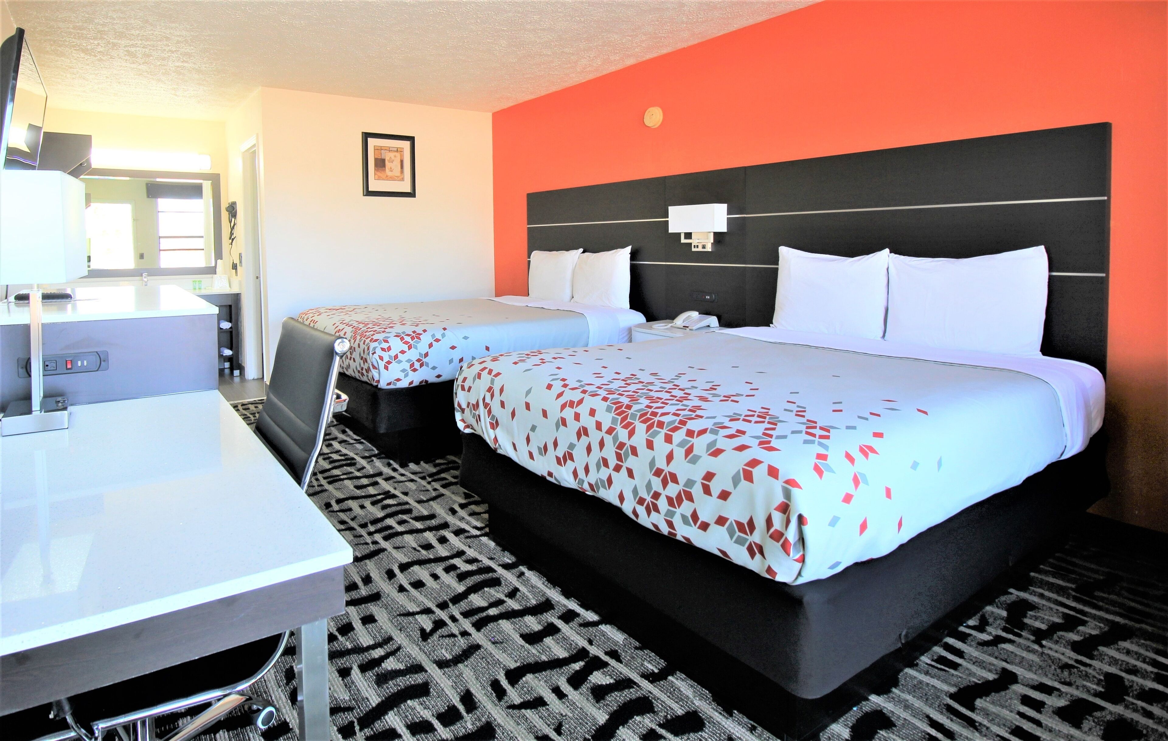 A hotel room with two beds, a desk, a chair, a TV, and a bathroom.