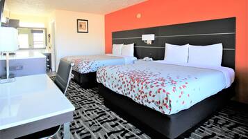 A hotel room with two beds, a desk, a chair, a TV, and a bathroom.