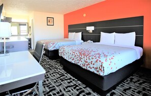 A hotel room with two beds, a desk, a chair, a TV, and a bathroom.