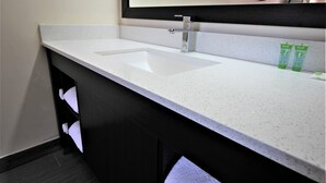 Un baño con encimera blanca con motas, un grifo cromado y dos botellas verdes de champú.