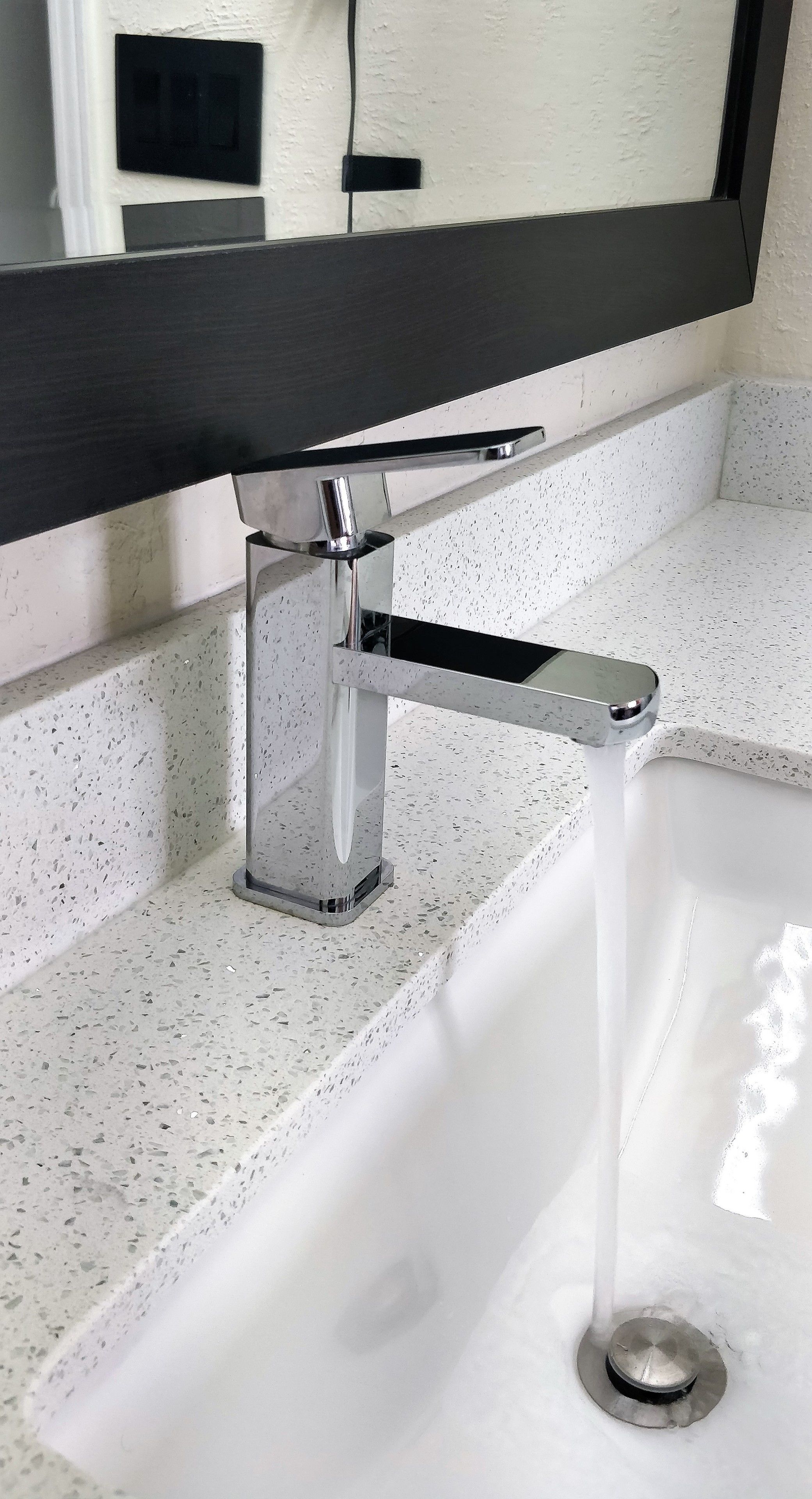 A modern bathroom with a white speckled countertop, a chrome faucet, and a mirror above the sink.
