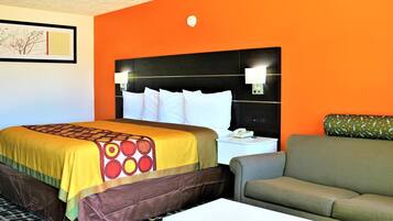 Habitación de hotel con una pared naranja, una cama con colcha estampada, un cabecero con luces, un sofá verde y una mesita de noche con un teléfono.