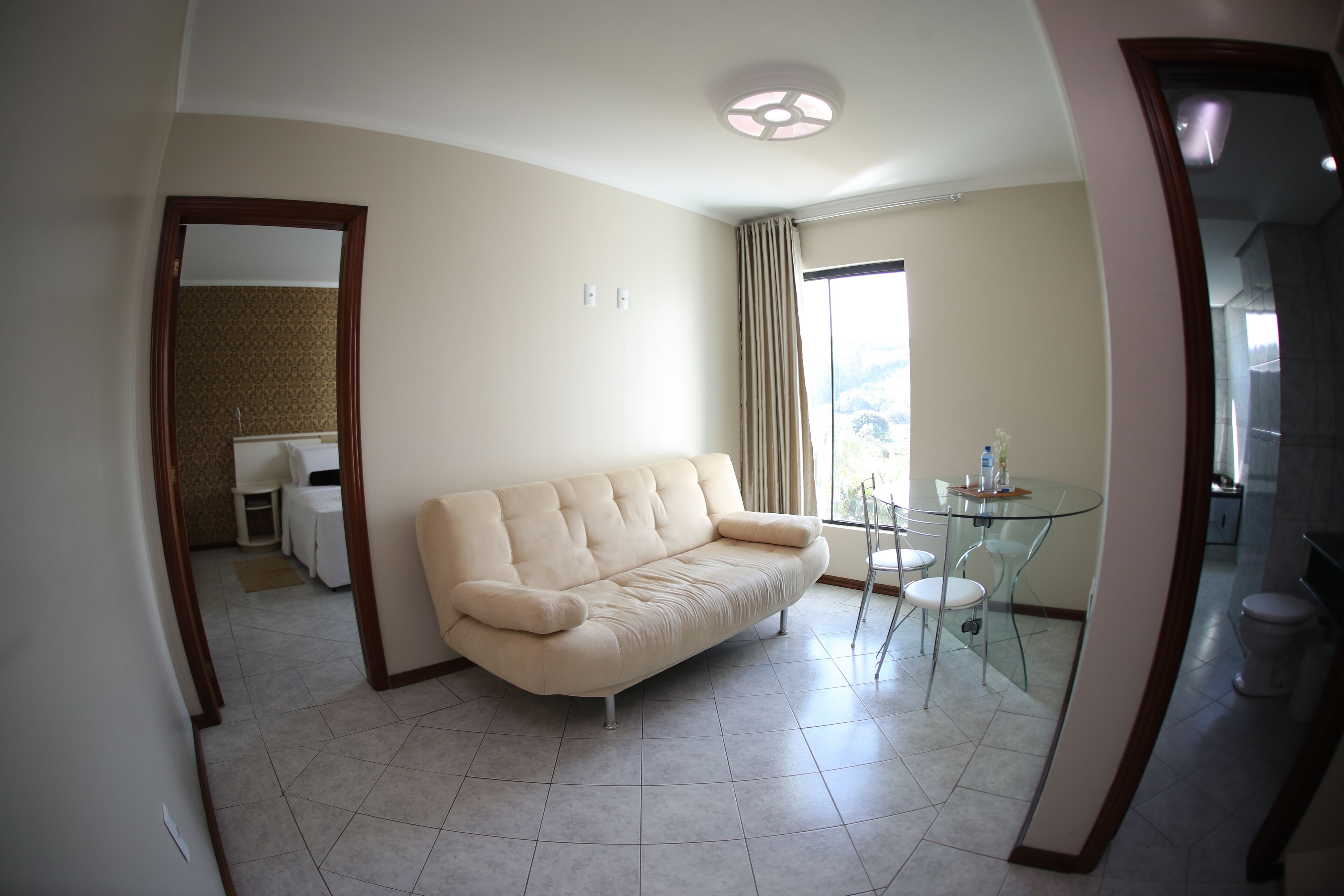 A modern living room with a beige sofa, a glass table, and a view of the outdoors.