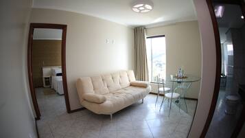 A modern living room with a beige sofa, a glass table, and a view of the outdoors.