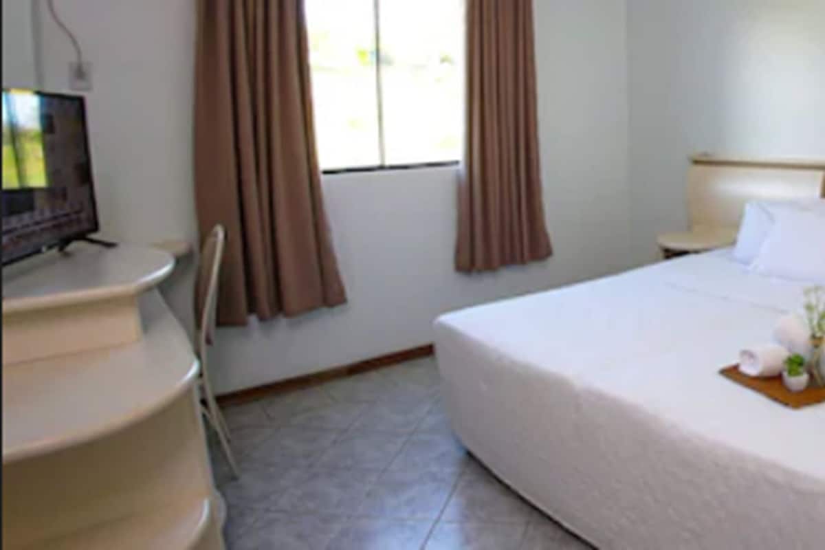 Una habitación de hotel con una cama, una mesita de noche, un televisor y cortinas.