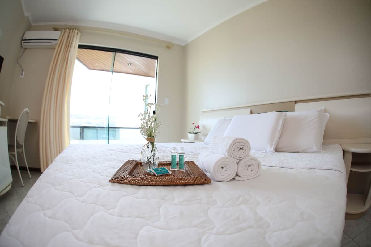 Habitación de hotel con una cama grande, una mesita de noche con lámpara, una ventana con cortinas y vistas al exterior.