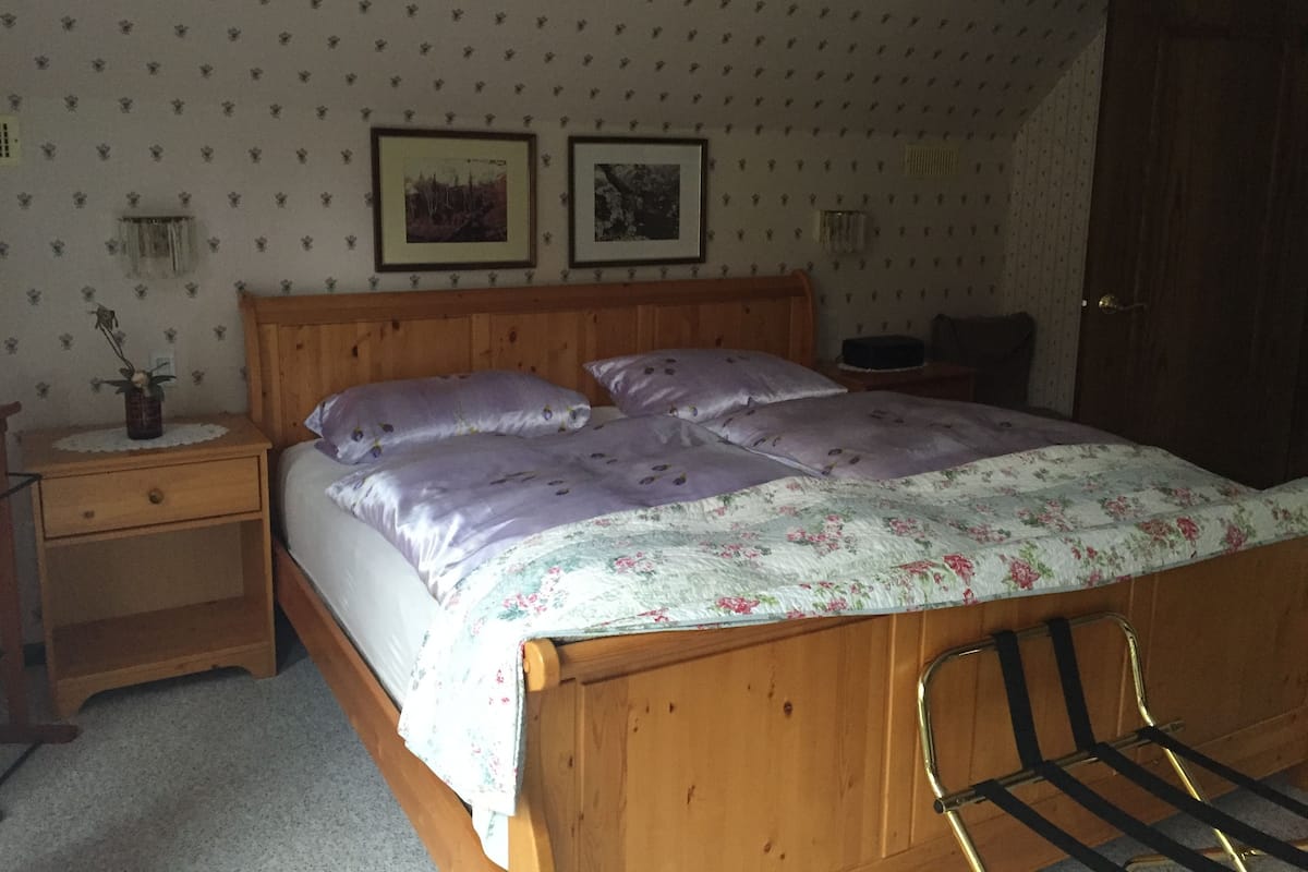 A bedroom with a wooden bed, a nightstand, a bedside table with a vase, and two framed pictures on the wall.