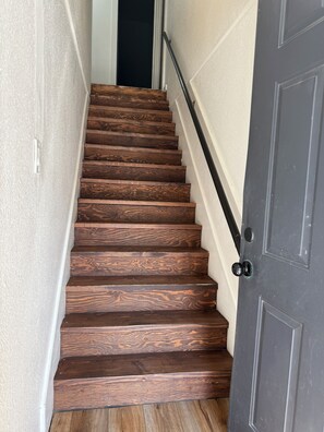 Un escalier en bois avec une rampe noire menant à une porte sombre.