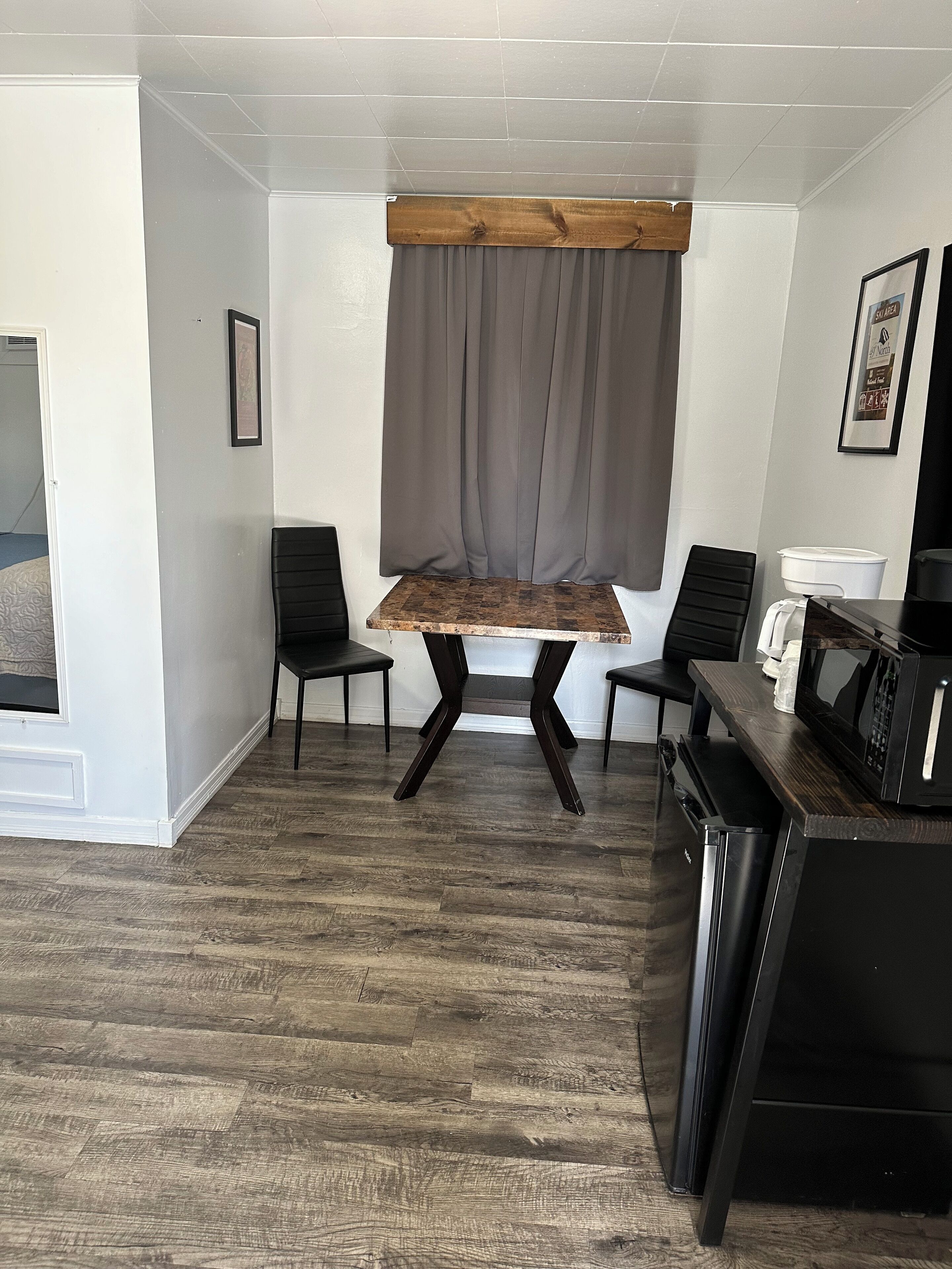 A small, modern room with a wooden table, two black chairs, a microwave, and a refrigerator.