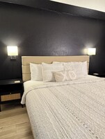 Una cama bien tendida con ropa de cama estampada, un cabecero y dos mesitas de noche con lámparas.