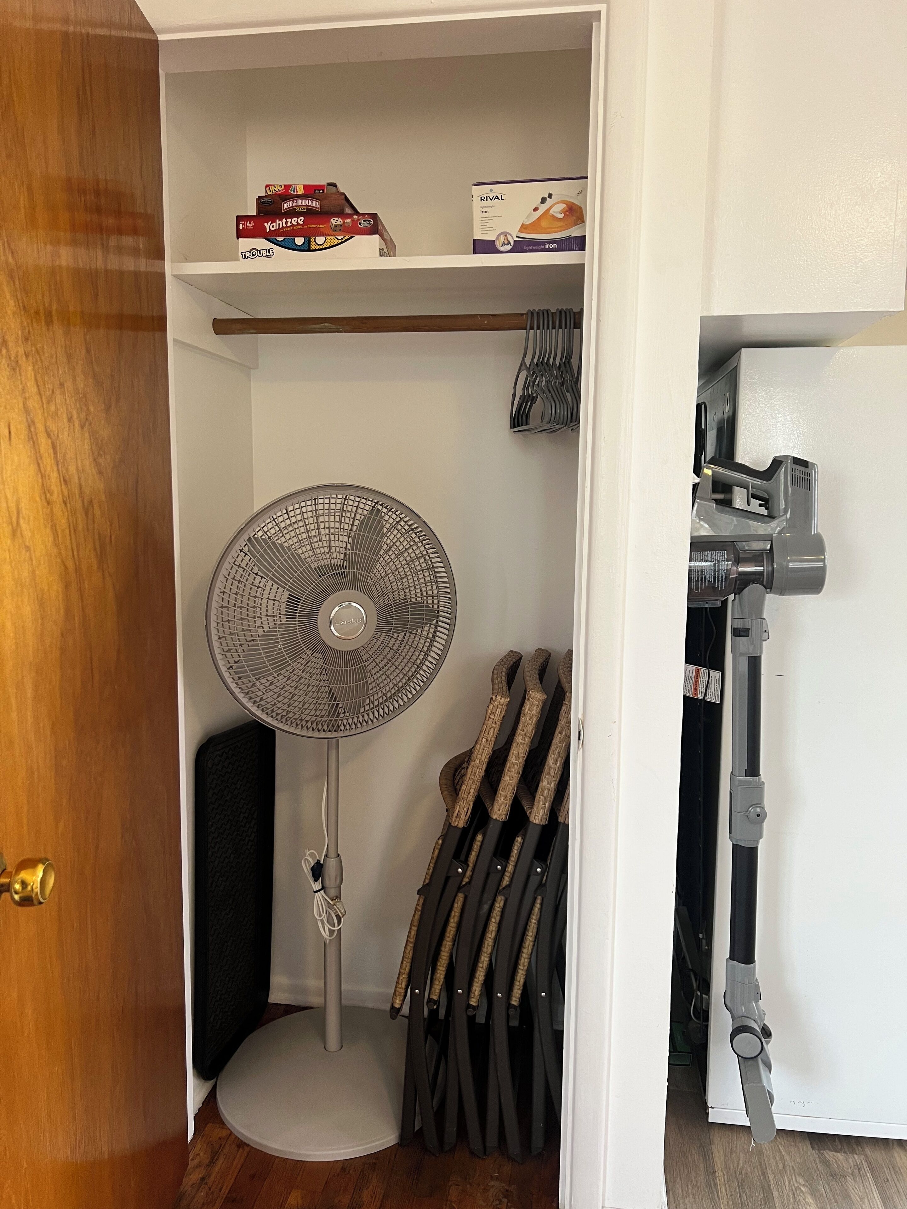 A compact room with a standing fan, a shelf with boxes, and a vacuum cleaner.