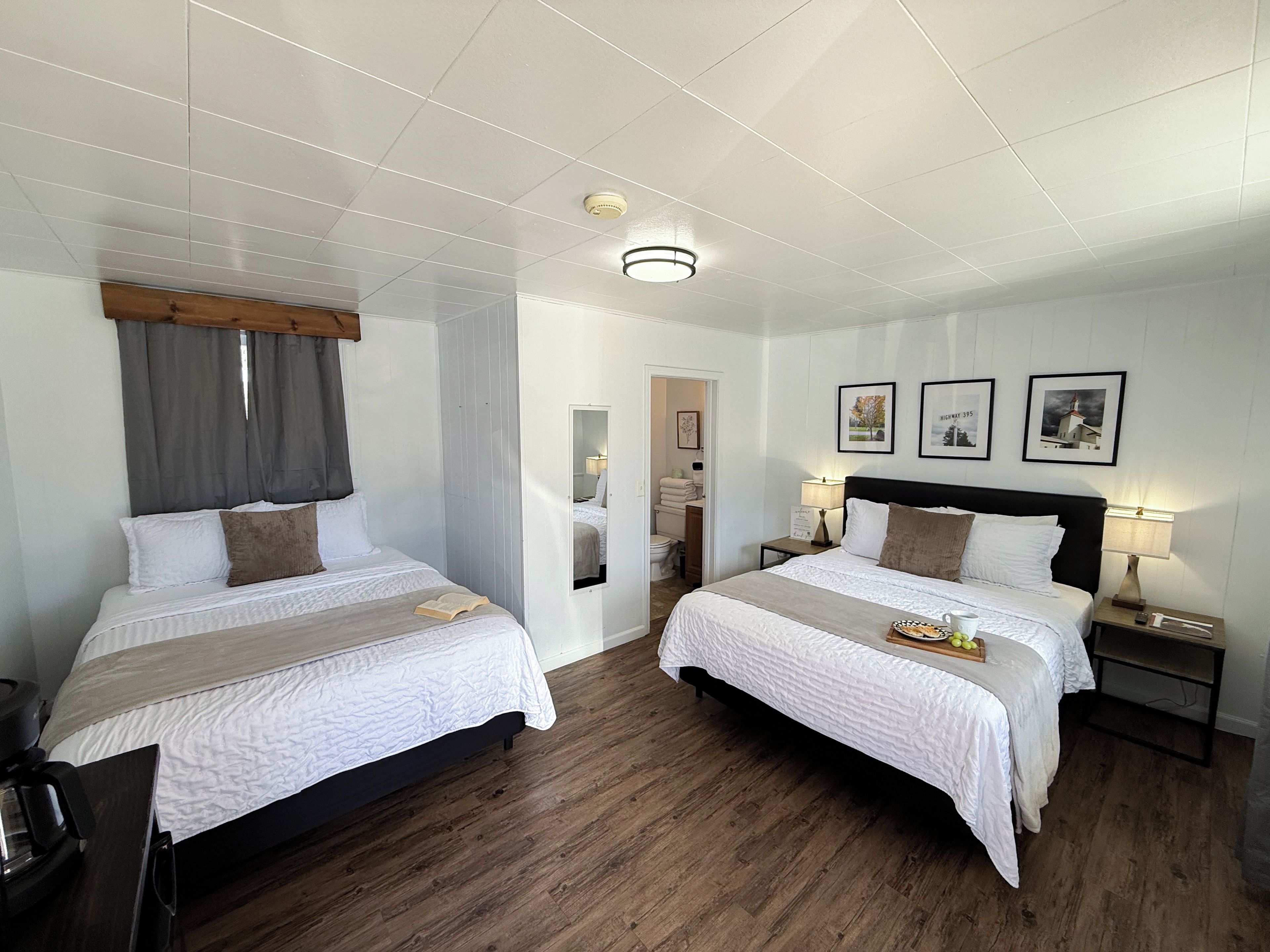 Habitació d'hotel amb dos llits, terres de fusta, una làmpada al sostre i quadres a la paret.