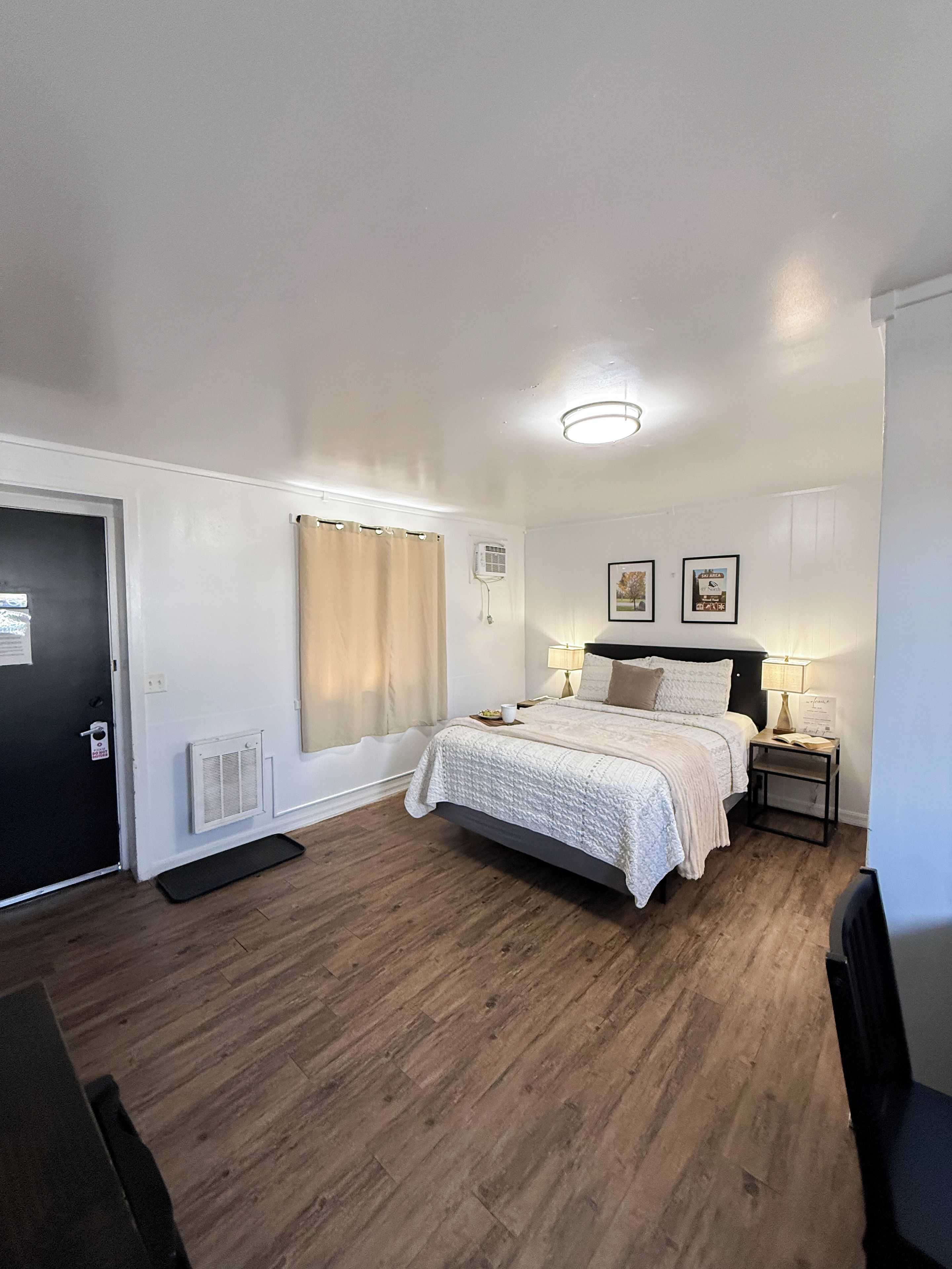 A bedroom with a bed, bedside tables, a door, and a window with curtains.