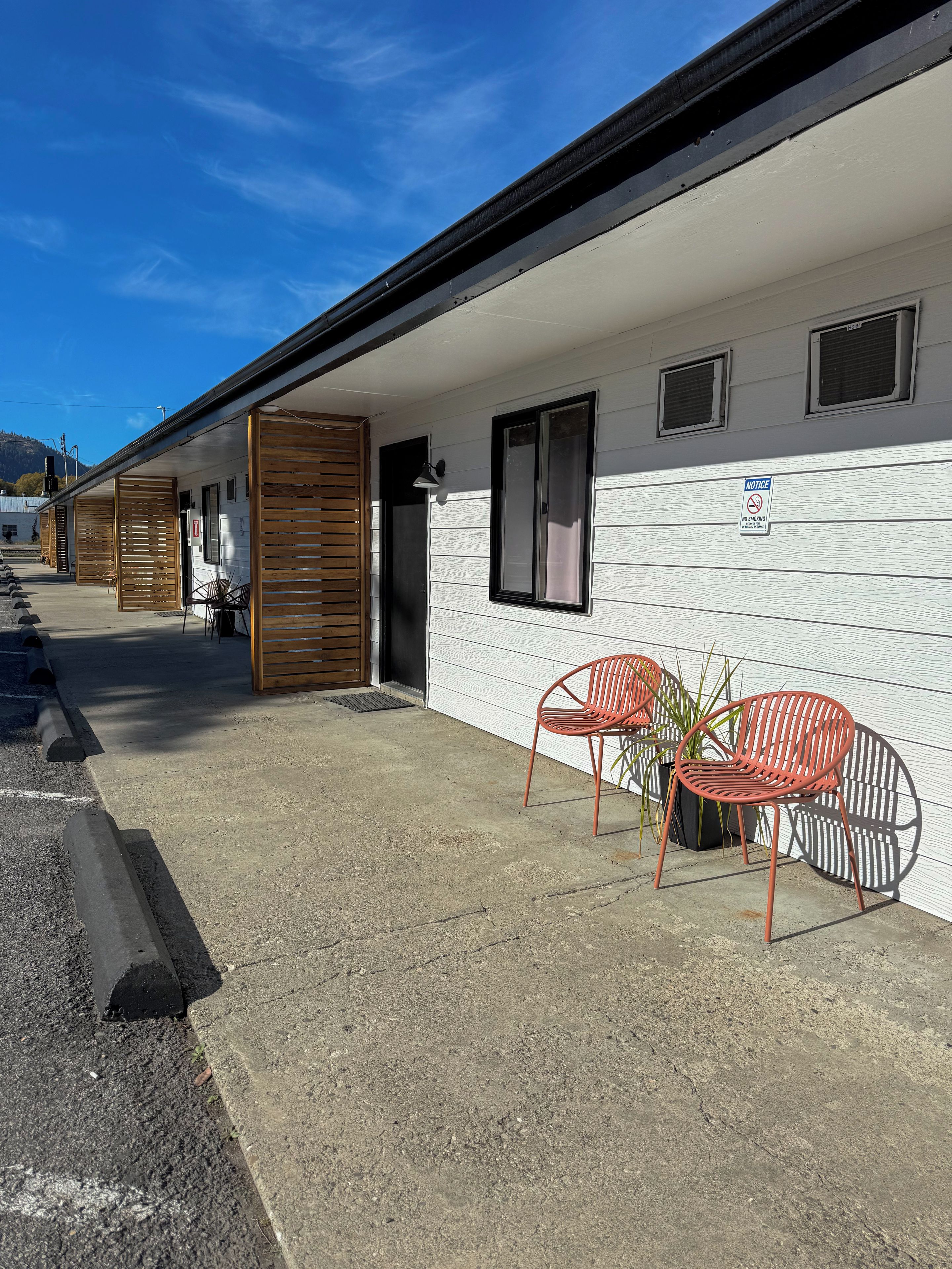 A motel with a covered outdoor seating area, a no-smoking sign, and a view of the mountains in the background.