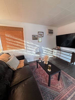 Uma sala de estar moderna com um sofá de couro preto, uma mesa de centro, uma televisão e um tapete estampado.