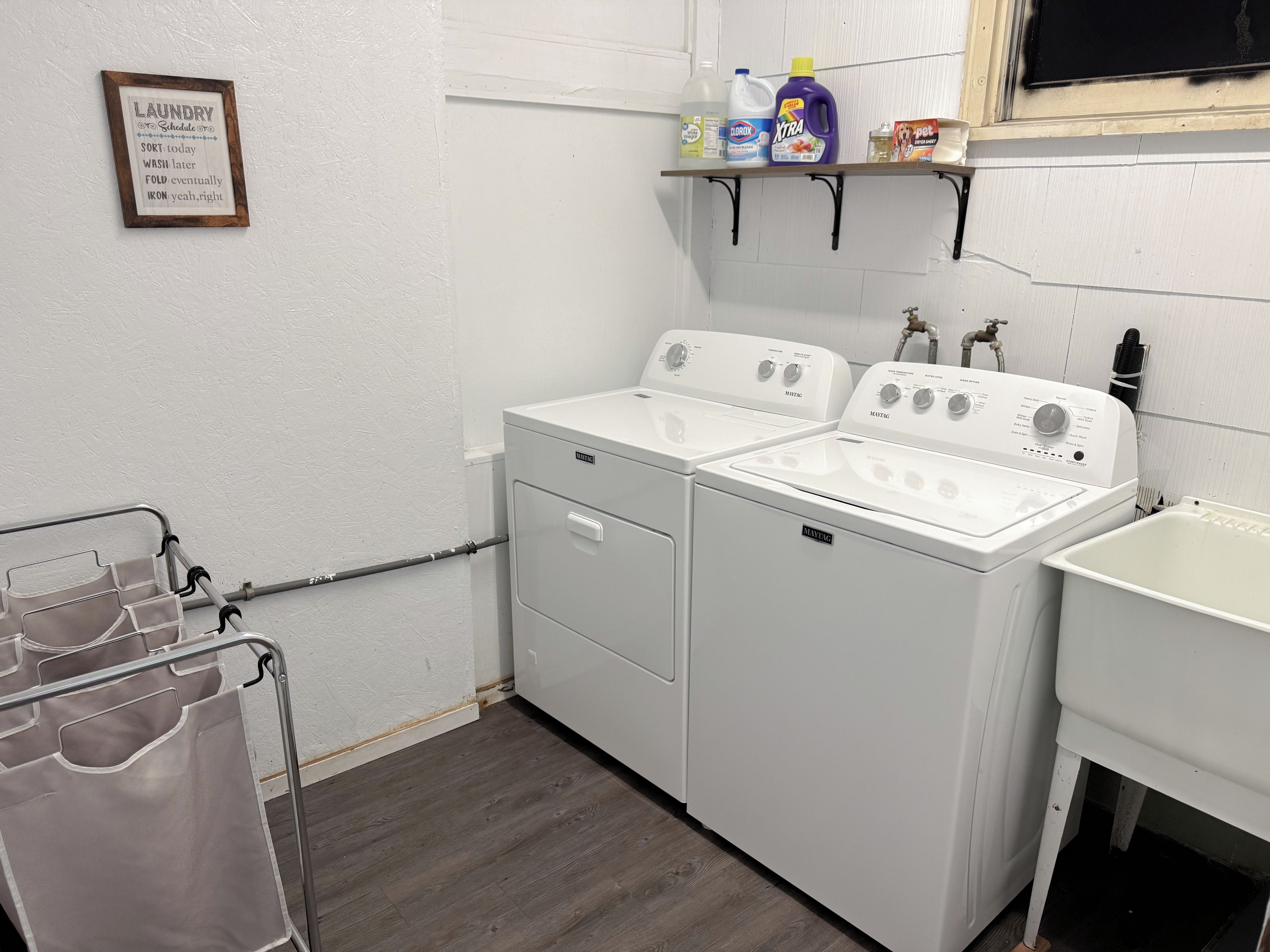 A laundry room with a Maytag washer and dryer, a shelf with cleaning supplies, and a laundry cart.