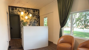 A modern room with a wooden floor, a white reception desk, two leather chairs, and a large window with a view of trees.