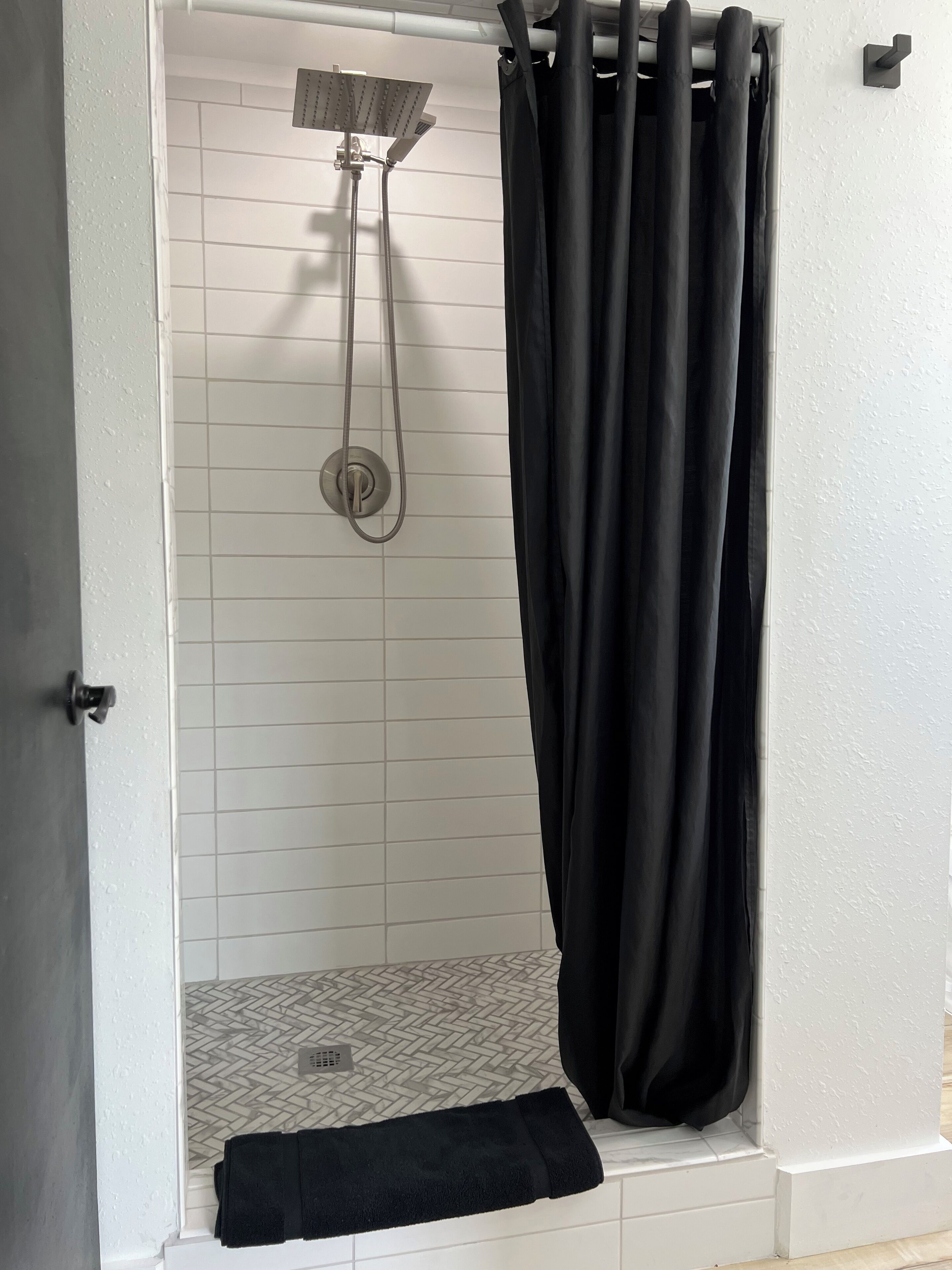 A shower area with a showerhead, a black curtain, and a tiled floor.