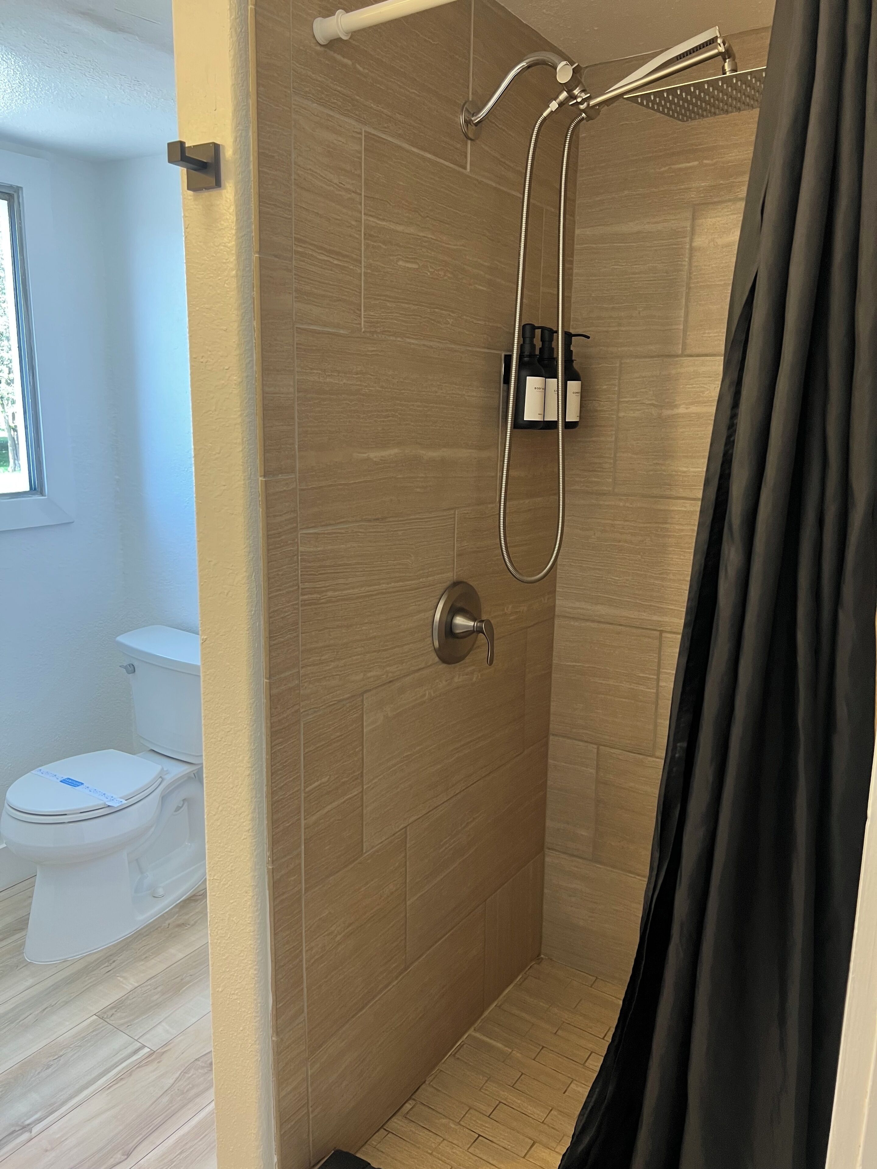 A modern bathroom with a shower, toilet, and a window.