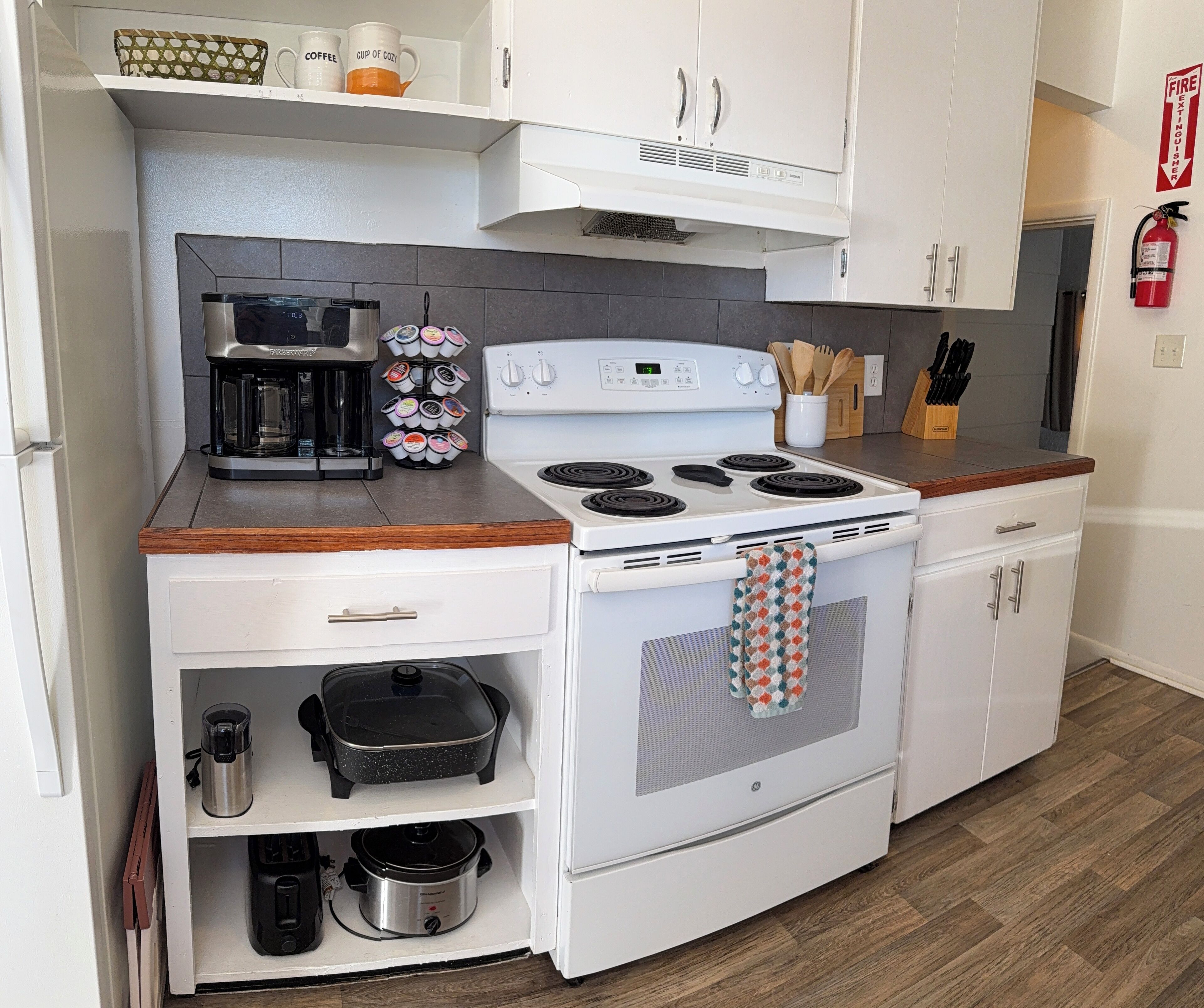 A compact kitchen with white cabinets, a stove, a coffee maker, and a crockpot.