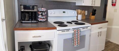 A compact kitchen with white cabinets, a stove, a coffee maker, and a crockpot.
