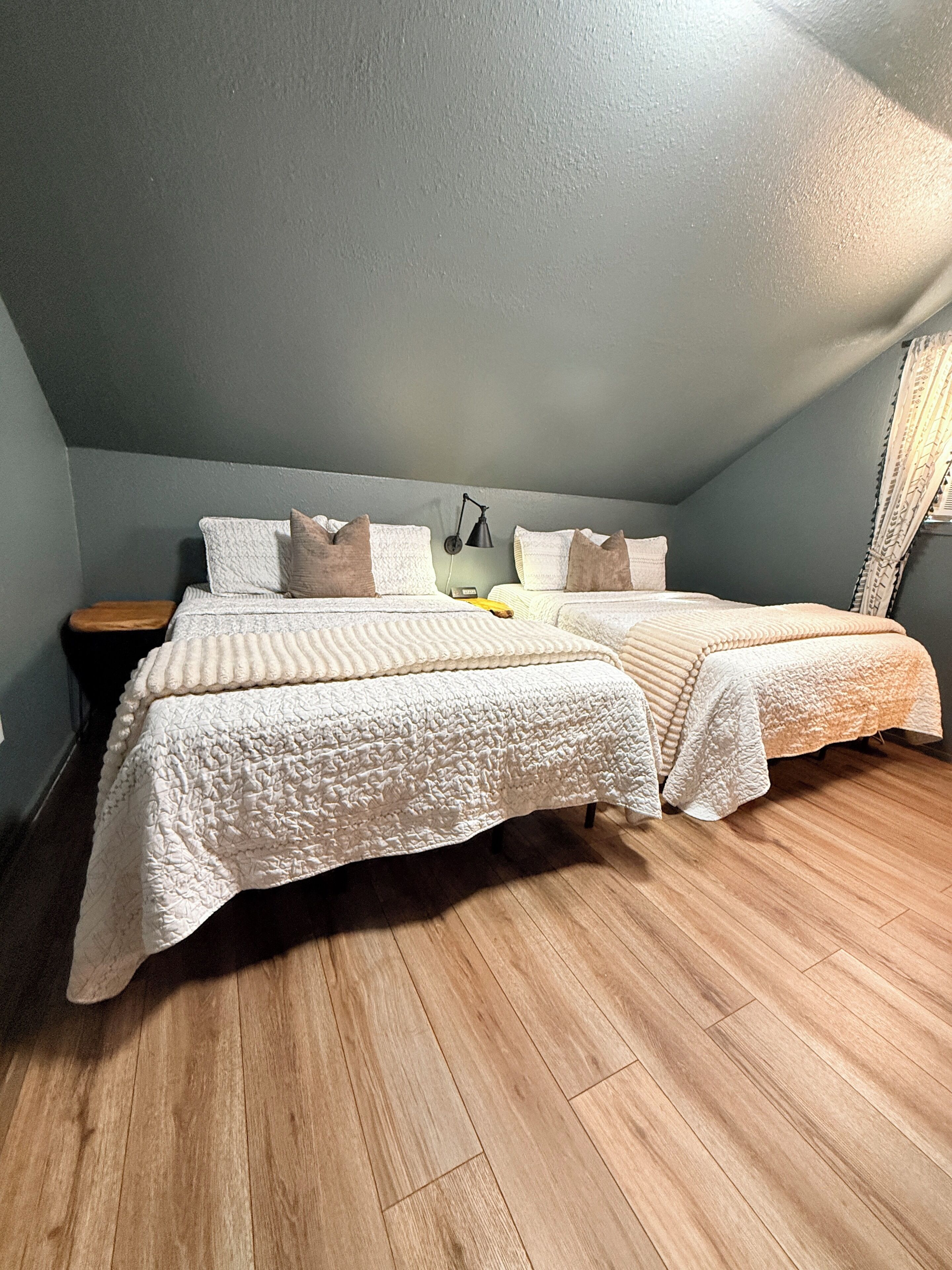 A bedroom with two beds, a nightstand, a lamp, and a wooden floor.