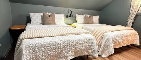 A bedroom with two beds, a nightstand, a lamp, and a wooden floor.