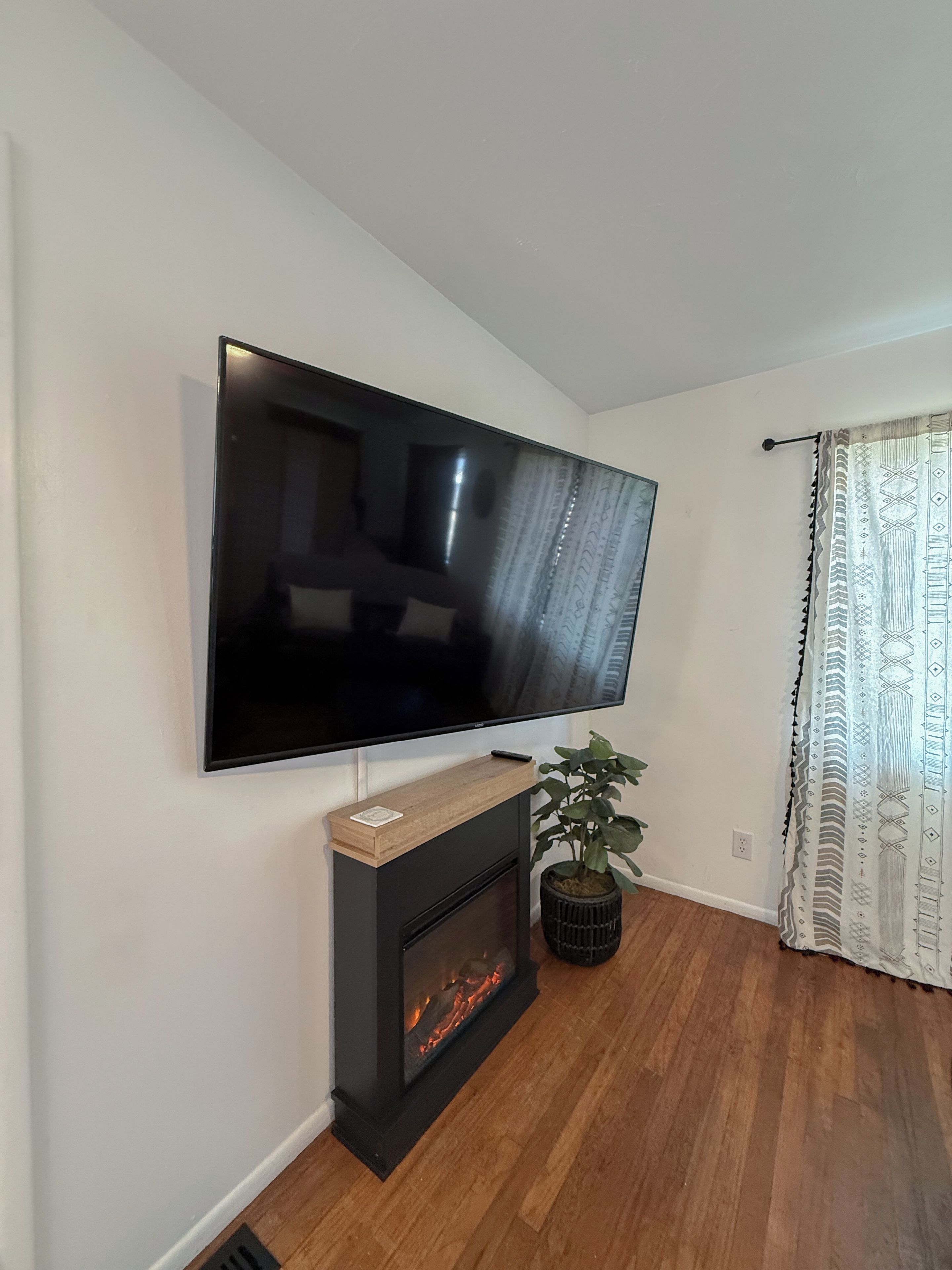 Televisão de tela plana presa na parede acima de uma lareira, com um controle remoto sobre a peça decorativa.