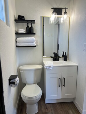 Une salle de bain avec des toilettes, des meubles blancs, un miroir et une étagère où sont rangées des serviettes et des articles de toilette.