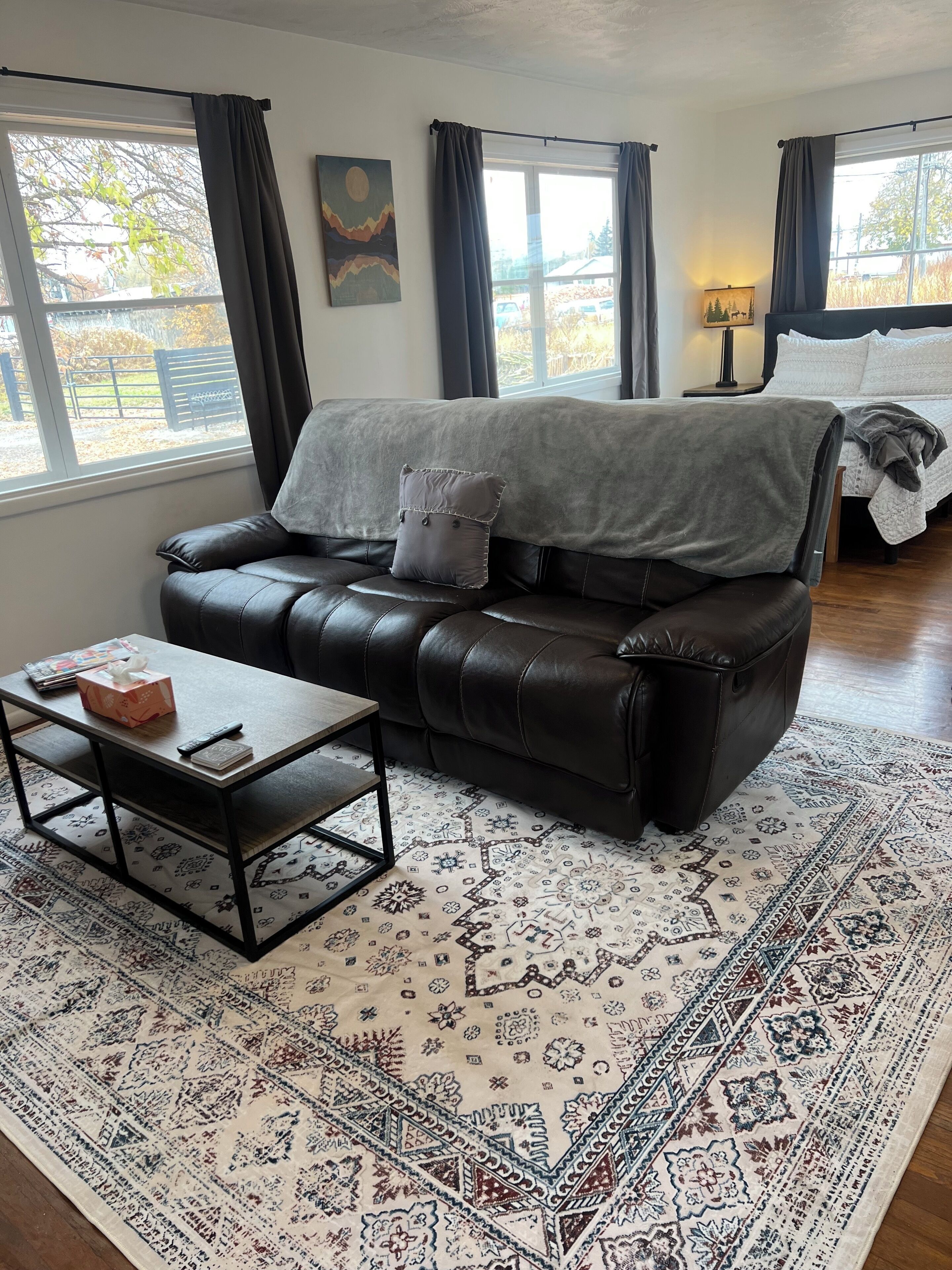 Un salon avec un canapé en cuir noir, une table basse en bois et un tapis à motifs.