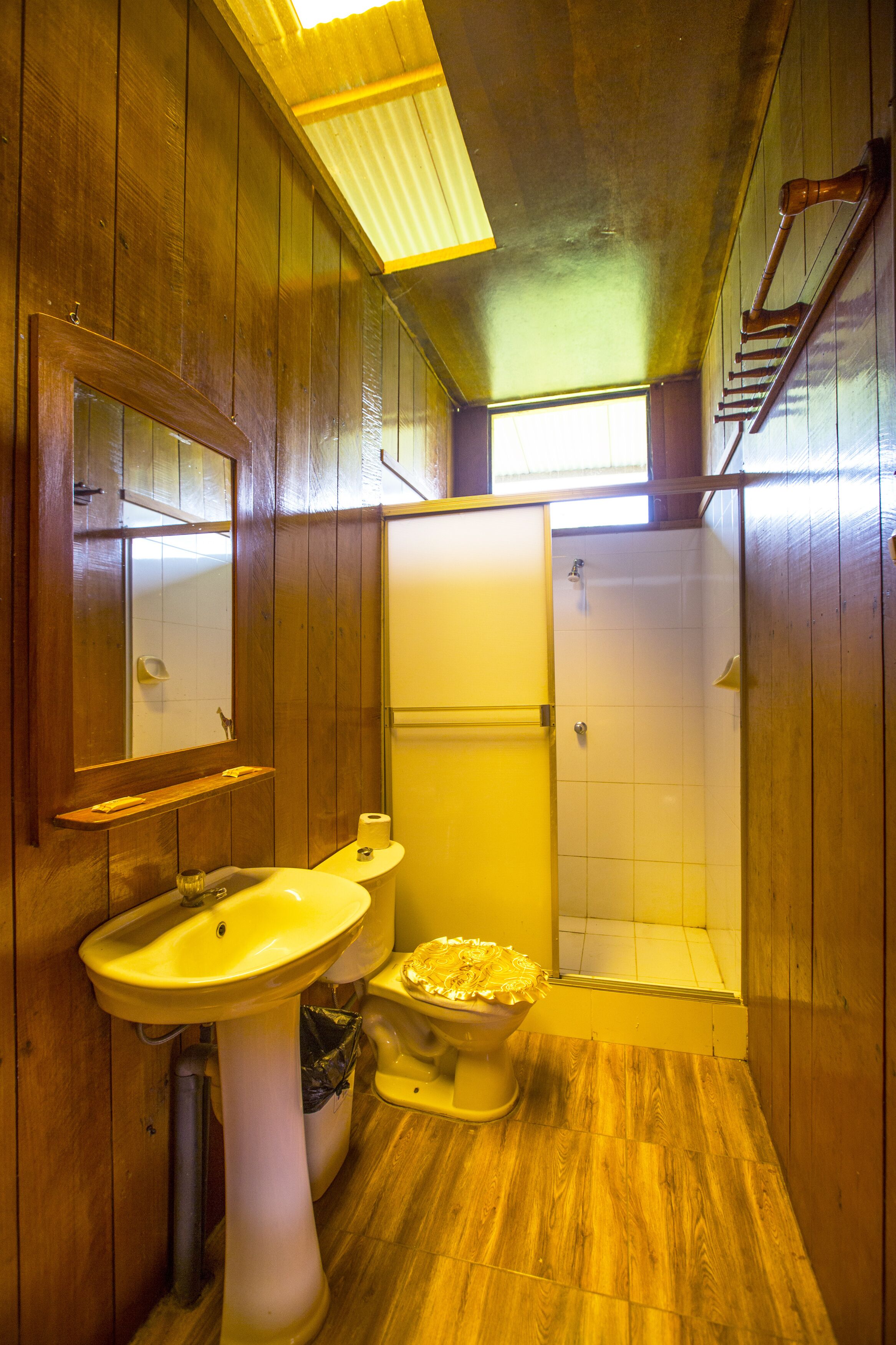 A bathroom with wooden walls, a white sink, a toilet, and a shower area.
