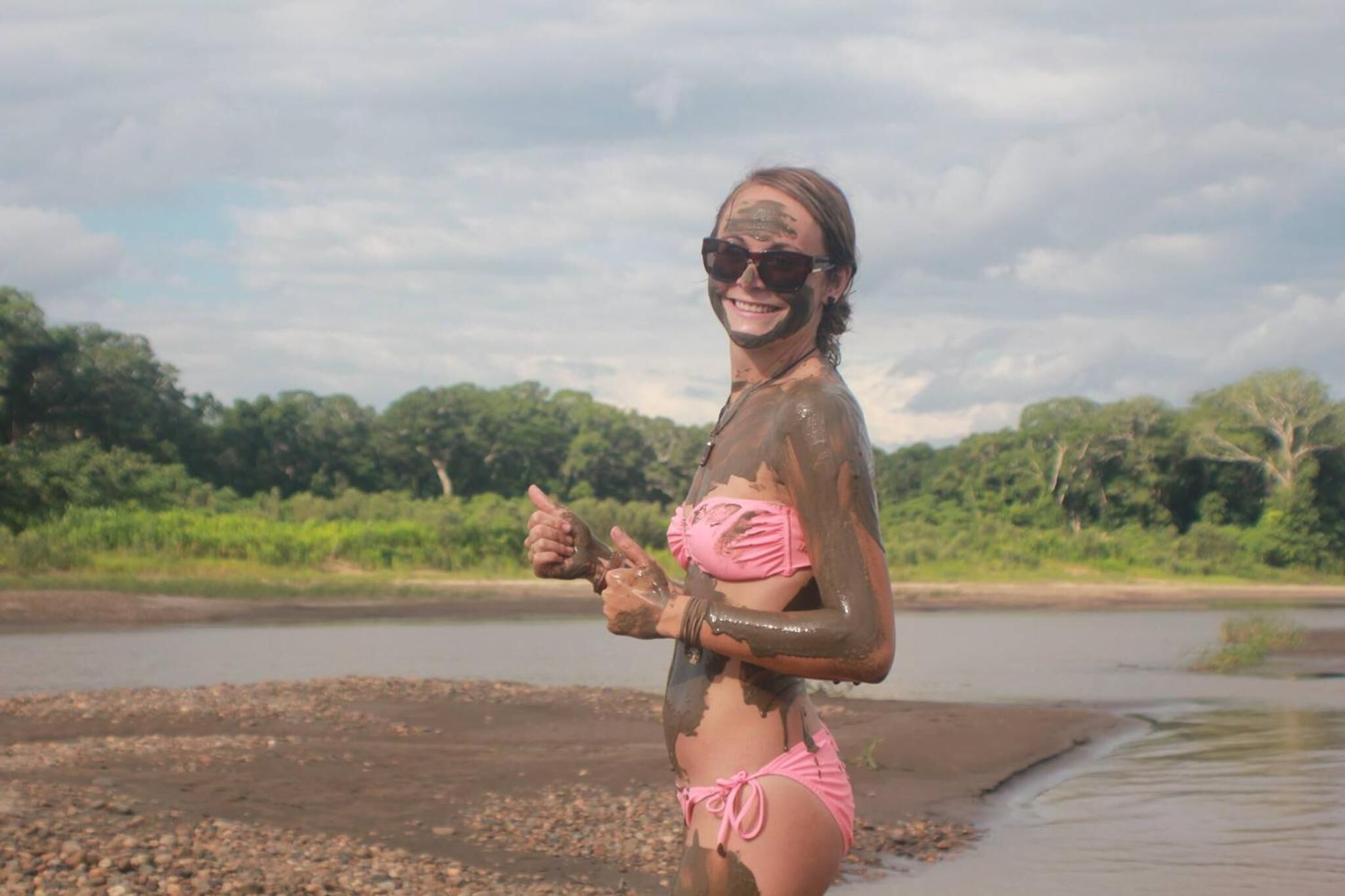 A person standing by a river with trees in the background.