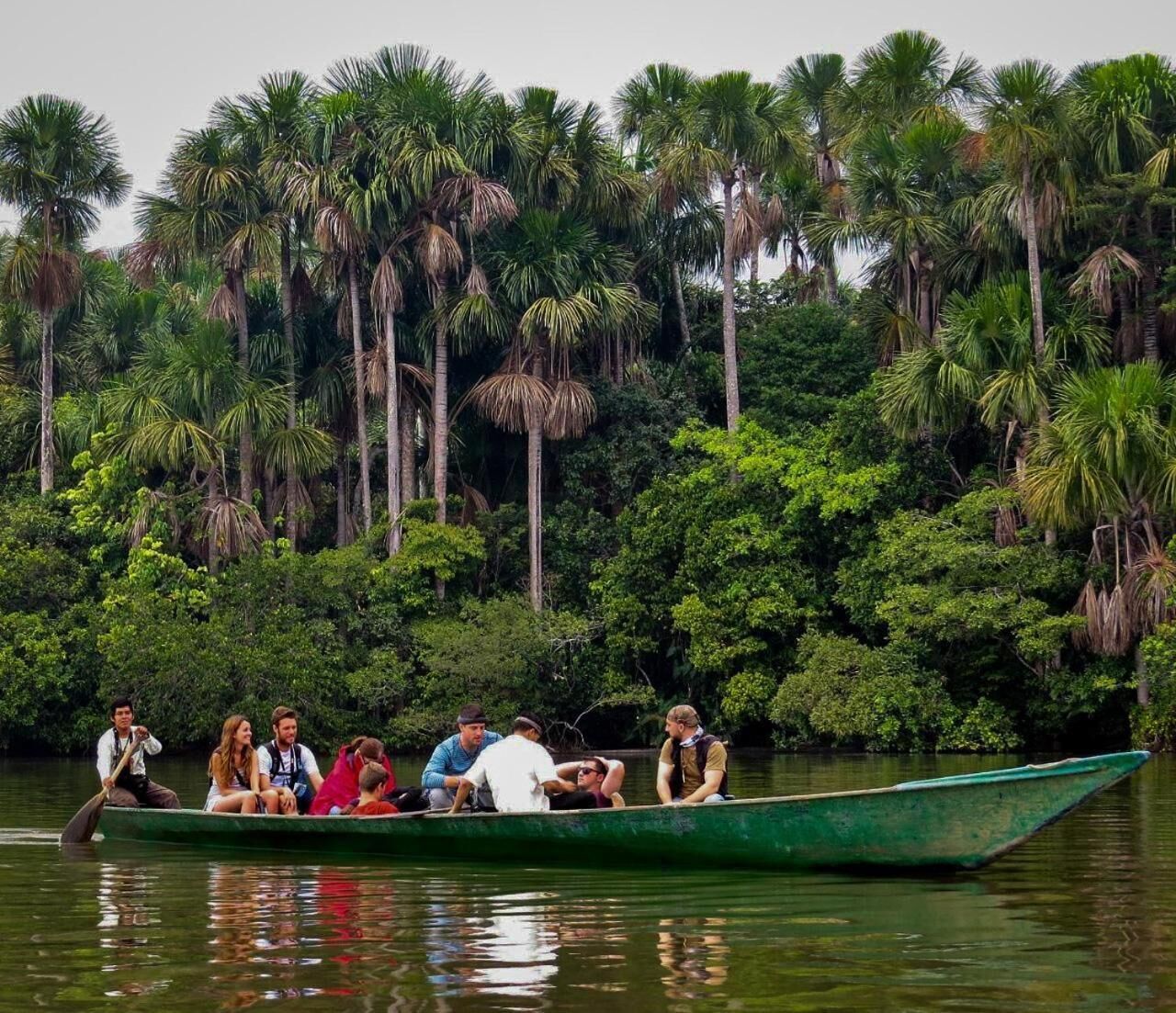 A group of people in a green boat on a river surrounded by dense tropical foliage.