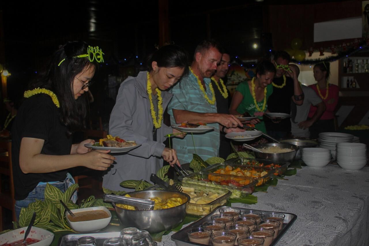 A buffet setup with various food items and people serving themselves.