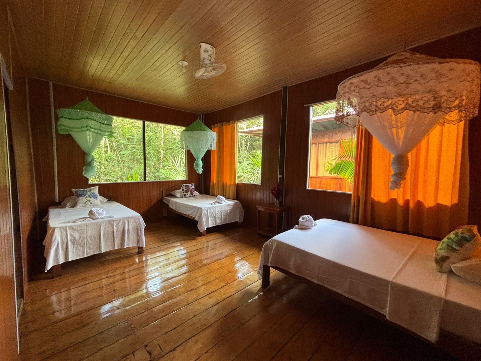 A room with wooden floors, two single beds, a small table, and a window with curtains.