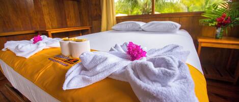 Una cama con sábanas blancas, una colcha amarilla y toallas con estampado de flores rosadas.