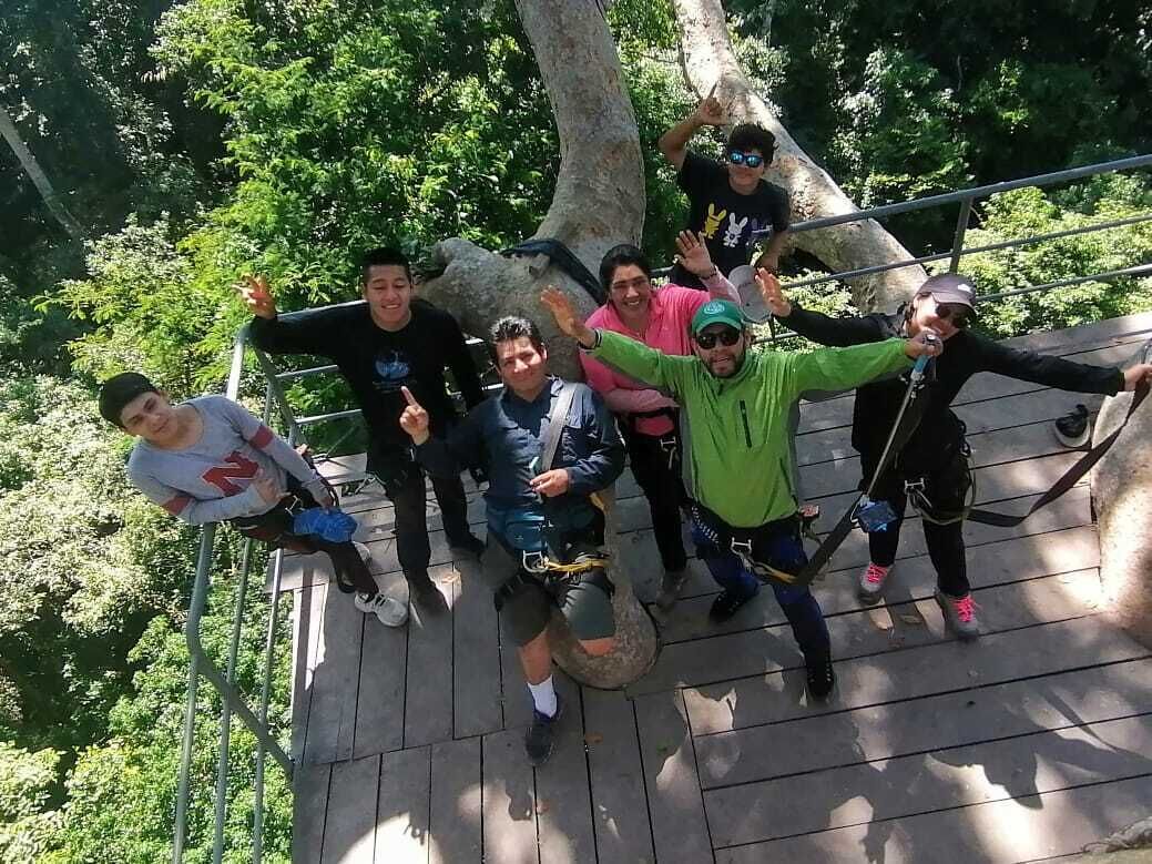 Un grupo de personas en una plataforma de madera con barandales de metal, rodeadas de árboles.