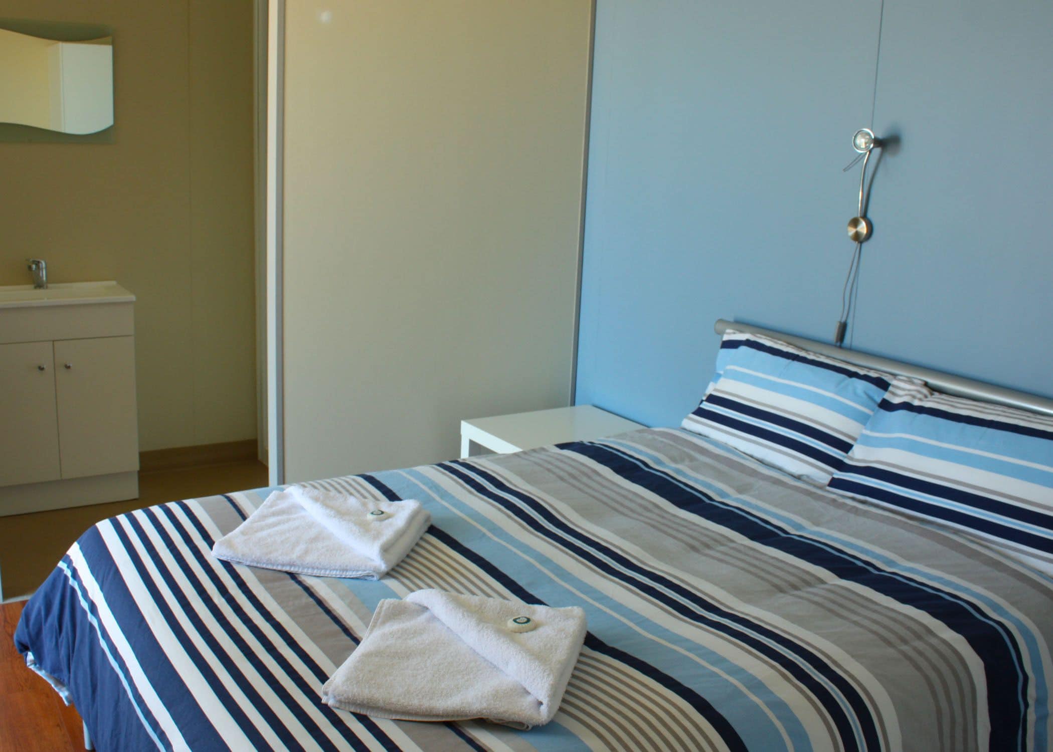 Una cama bien hecha con ropa de cama a rayas y dos toallas dobladas.