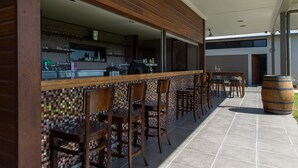 Un área de bar al aire libre con sillas de madera y piso de baldosas, una barra y un barril grande.