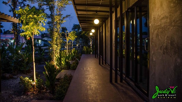 Un camino que lleva a un edificio con ventanas amplias y un área techada con luces colgantes.