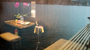 A room with a view of the water, a table with a bottle of champagne, a bottle of water, and a vase with flowers.