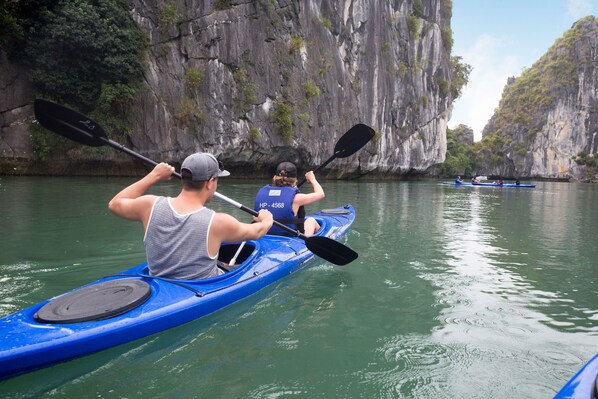 A person kayaking on a river with rocky cliffs on one side.