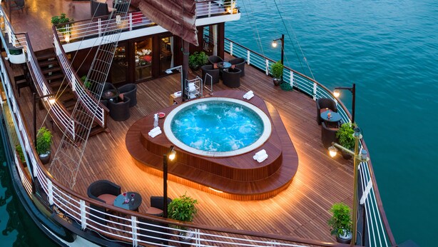 A luxurious cruise ship with a hot tub surrounded by seating and potted plants, set against a calm sea backdrop.