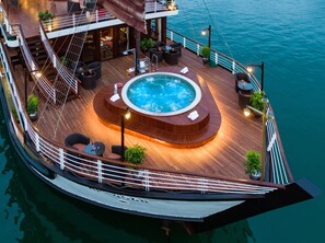 A luxurious cruise ship with a hot tub surrounded by seating and potted plants, set against a calm sea backdrop.
