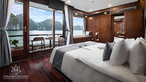 A spacious bedroom with a large bed, a balcony with a view of the sea, and a TV mounted on the wall.